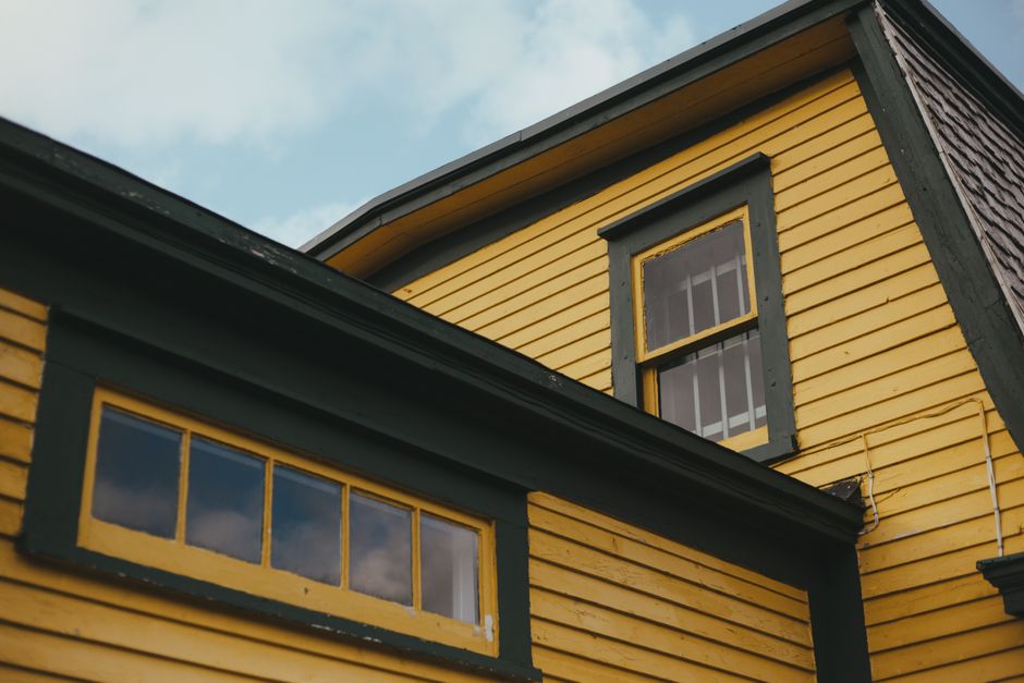 Low angle shot of a vibrant yellow house with green trim, featuring classic architecture.
